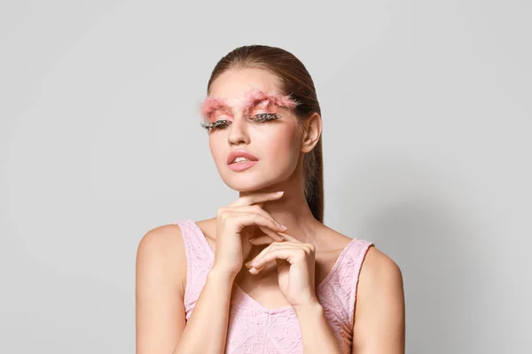 Mujer joven con pestañas y cejas creativas sobre fondo gris — Foto de Stock
