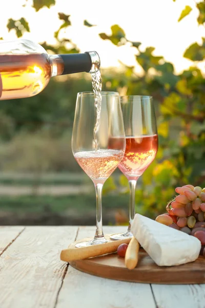 Gieten van smakelijke wijn uit fles in glazen op tafel met hapjes in wijngaard — Stockfoto