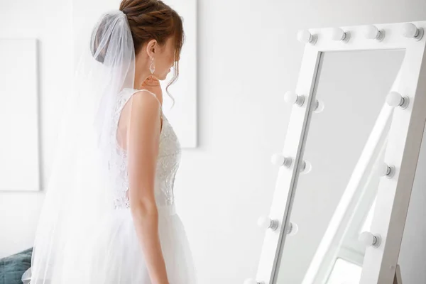Beautiful young bride near mirror before wedding ceremony at home — Stock Photo, Image