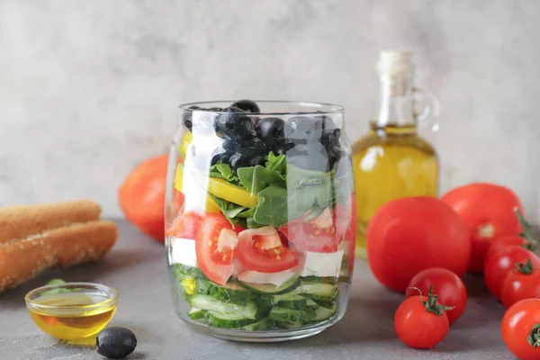 Glas mit leckerem griechischen Salat auf grauem Tisch — Stockfoto