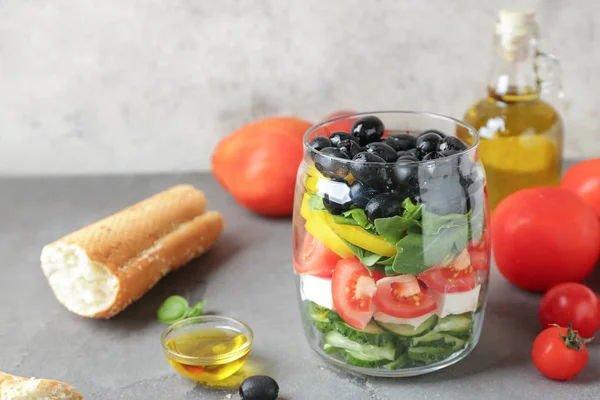 Glas mit leckerem griechischen Salat auf grauem Tisch — Stockfoto