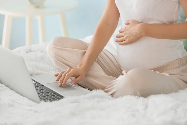 Красивая беременная женщина с ноутбуком сидит на кровати — стоковое фото