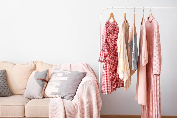 Scaffale con abiti femminili puliti e divano nello spogliatoio — Foto Stock