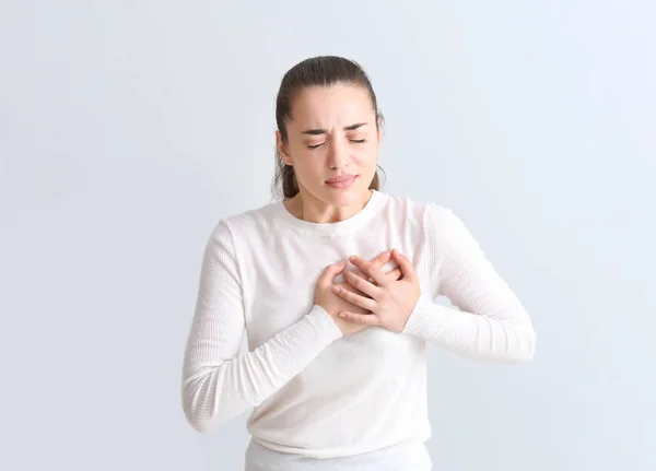 Junge Frau erleidet Herzinfarkt vor hellem Hintergrund — Stockfoto