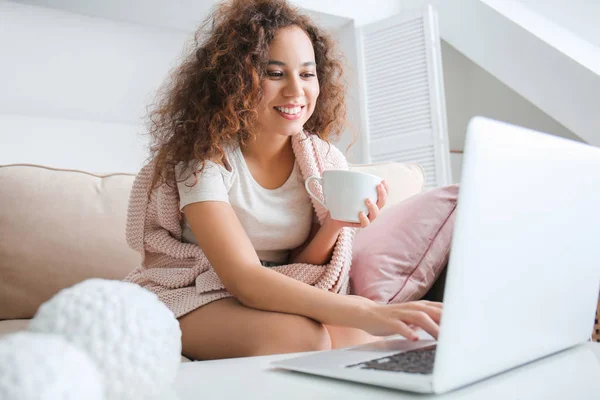 Beautiful young woman with laptop and cup of coffee at home — Stock Photo, Image