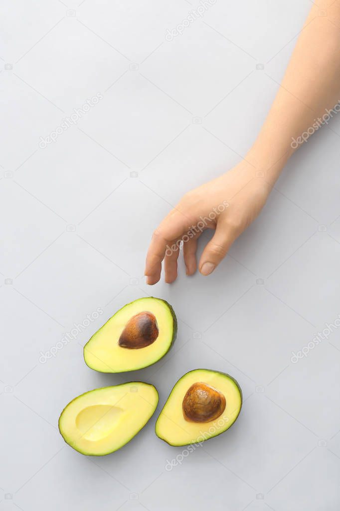 Female hand and halves of ripe avocado on white background