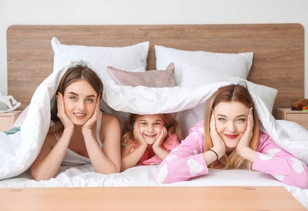 Happy lesbian couple with little daughter lying under blanket in bed — Stock Photo, Image