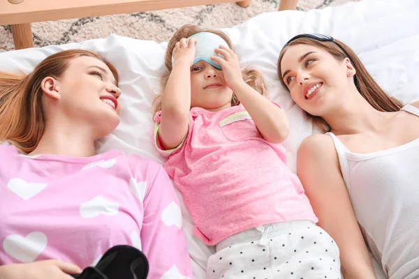 Happy lesbian couple with little daughter lying on bed — Stock Photo, Image