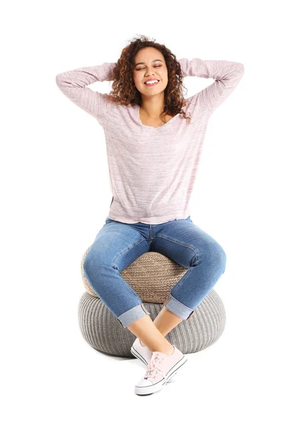 Beautiful African-American woman relaxing on poufs against white background — Stock Photo, Image