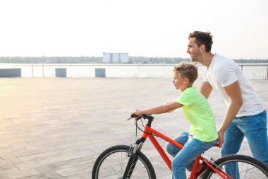 Baba oğluna dışarıda bisiklete binmeyi öğretiyor.