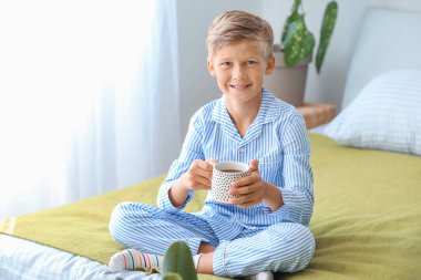Yatak odasında sıcak çikolata içen tatlı küçük çocuk.