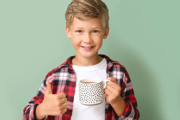 Happy little boy drinking hot chocolate on color background — ストック写真