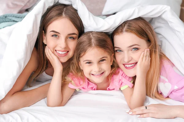 Happy lesbian couple with little daughter lying under blanket in bed — Stock Photo, Image