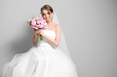 Gri arka planda düğün buketi olan güzel gelinin portresi