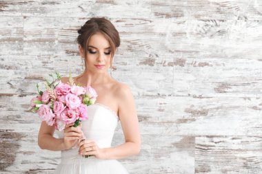 Ahşap arka planda düğün buketi olan güzel genç gelinin portresi.