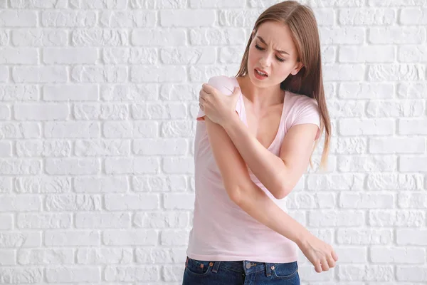 흰 벽돌 벽에 기대어 어깨에 통증을 느끼는 젊은 여자 — 스톡 사진