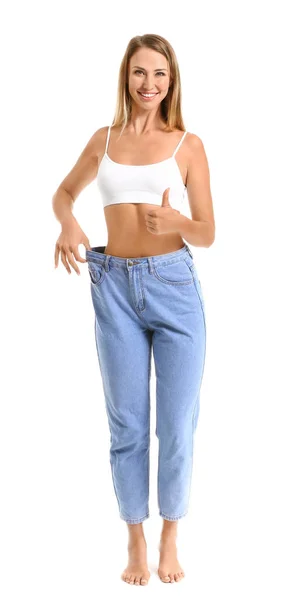 Mulher bonita em jeans soltos mostrando polegar para cima no fundo branco. Conceito de perda de peso — Fotografia de Stock