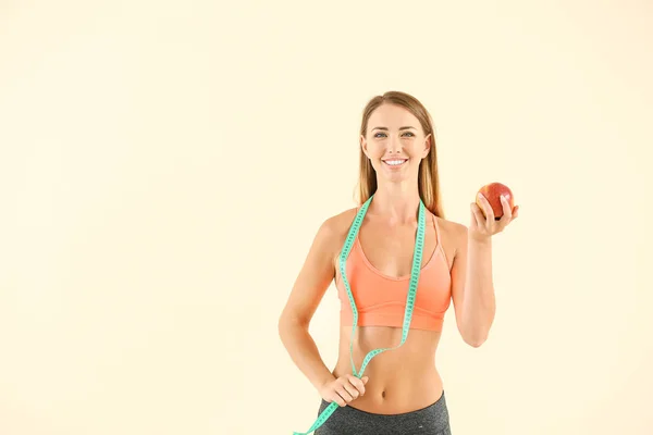 Красива спортивна жінка з мірною стрічкою та яблуком на кольоровому фоні. Концепція втрати ваги — стокове фото