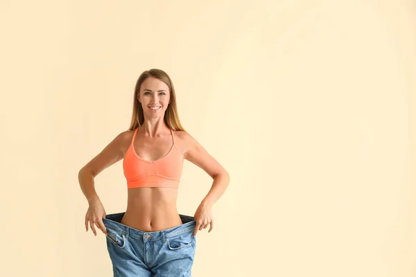 Schöne junge Frau in lockeren Jeans auf farbigem Hintergrund. Gewichtsverlust-Konzept — Stockfoto