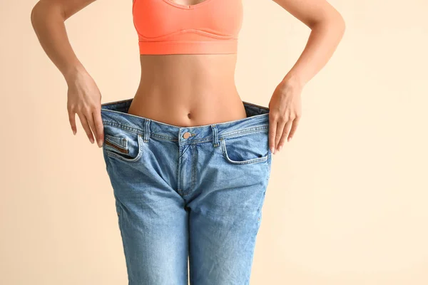Mulher bonita em jeans soltos no fundo de cor. Conceito de perda de peso — Fotografia de Stock