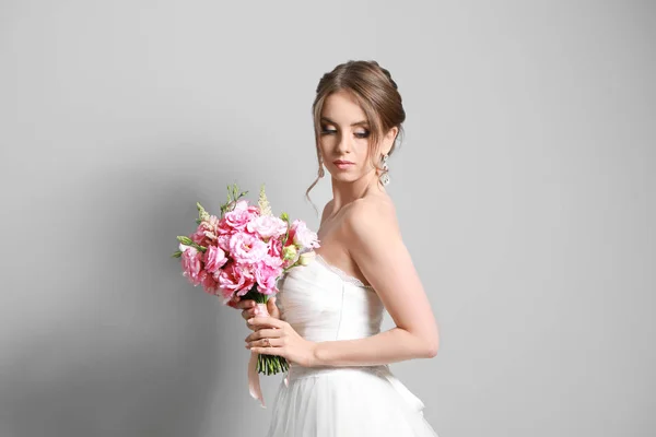 Porträt der schönen jungen Braut mit Brautstrauß auf grauem Hintergrund — Stockfoto