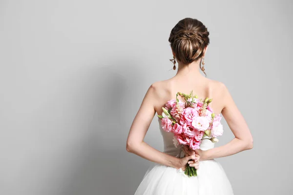 Beautiful young bride with wedding bouquet on grey background,  back view — Stock Photo, Image