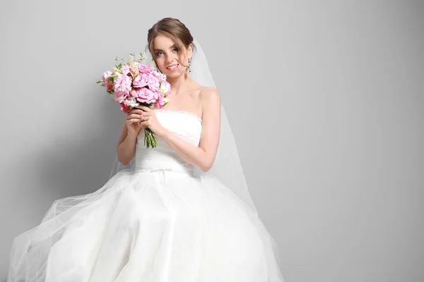 Portret van een mooie jonge bruid met bruidsboeket op grijze achtergrond — Stockfoto