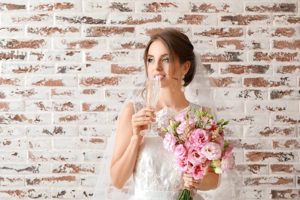 Portret van een mooie jonge bruid met bruidsboeket en glas champagne op bakstenen achtergrond — Stockfoto