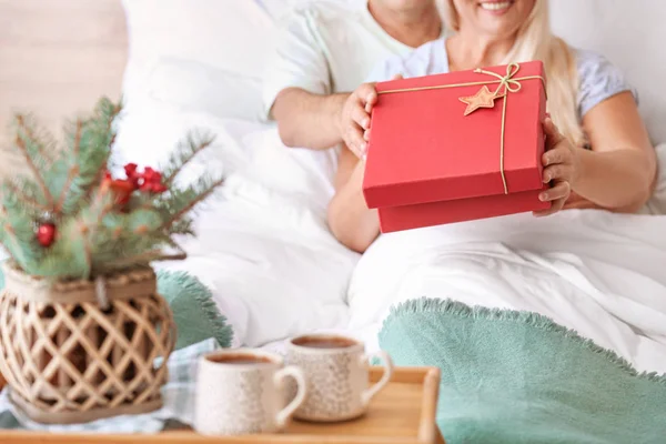 Äldre par med julklapp i sängen hemma — Stockfoto