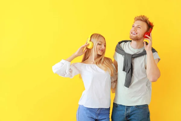 Young couple listening to music on color background