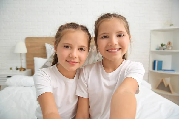 Portrait of twin girls taking selfie in bedroom — Stock Photo, Image