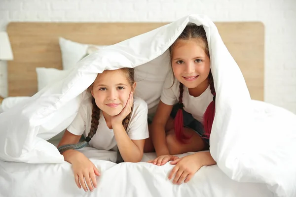 Portret bliźniaczek leżących pod kocem na łóżku — Zdjęcie stockowe