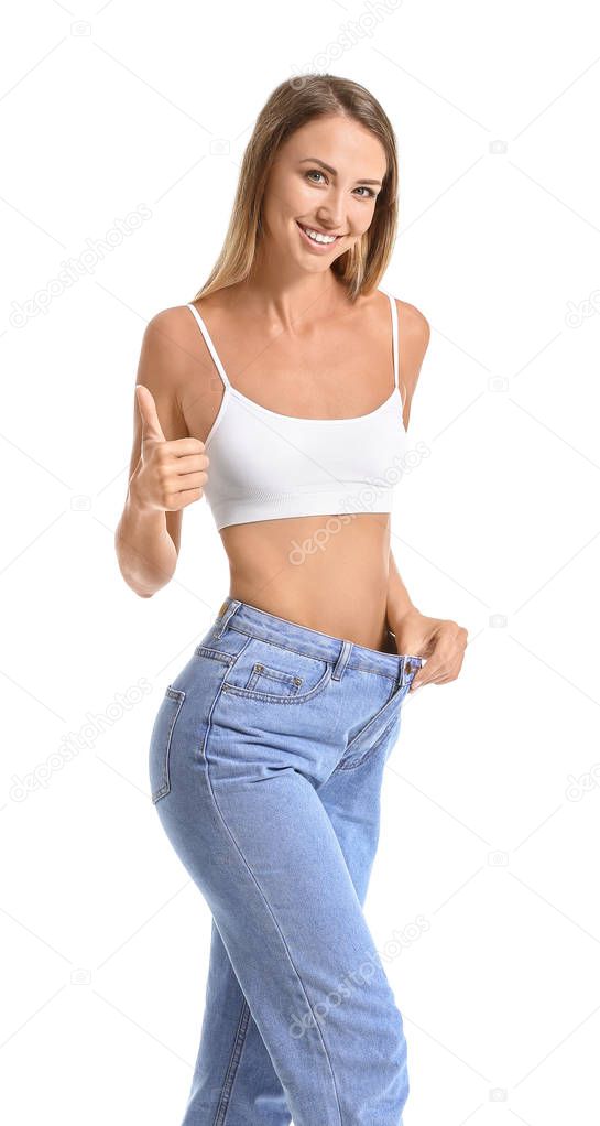 Beautiful young woman in loose jeans showing thumb-up on white background. Weight loss concept