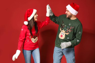 Noel süveteri ve Noel Baba şapkası giymiş genç bir çift birbirlerine renk geçmişiyle beşlik çakıyor.