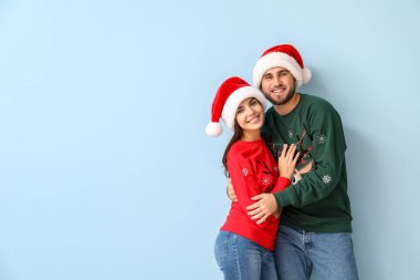 Mutlu çift, Noel süveteri ve Noel Baba şapkası giyiyor.