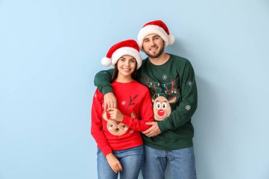 Mutlu çift, Noel süveteri ve Noel Baba şapkası giyiyor.