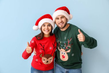 Noel süveteri ve Noel Baba şapkası giyen mutlu çift renk arka planında başparmak kaldırıyor.