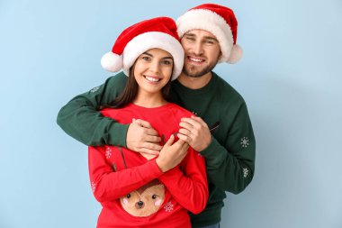 Mutlu çift, Noel süveteri ve Noel Baba şapkası giyiyor.