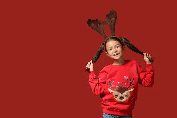 Cute girl in Christmas sweater and with deer horns on color background — Stock Photo, Image