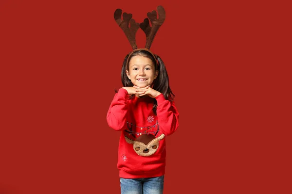 Cute girl in Christmas sweater and with deer horns on color background — Stock Photo, Image