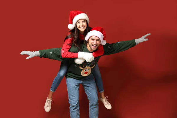 Young couple in Christmas sweaters and Santa hats on color background — Stock Photo, Image