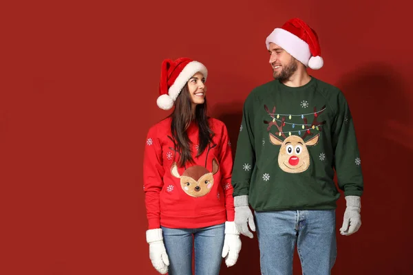 Молода пара в різдвяних светрах і Санта-капелюхах на кольоровому фоні — стокове фото