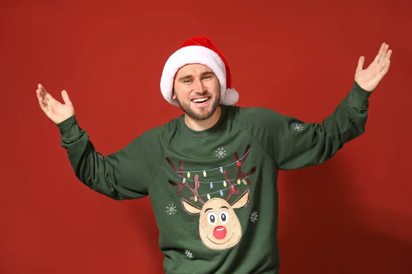 Young man in Christmas sweater and Santa hat on color background — Stock Photo, Image