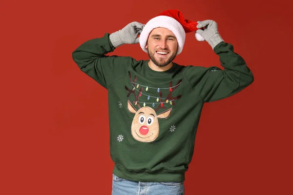 Young man in Christmas sweater and Santa hat on color background — Stock Photo, Image