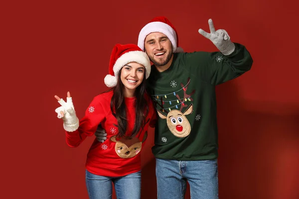 Νεαρό ζευγάρι σε χριστουγεννιάτικα πουλόβερ και καπέλα Σάντα στο φόντο χρώμα — Φωτογραφία Αρχείου