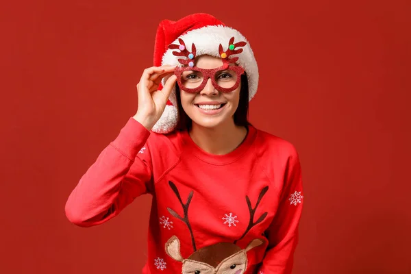 Funny woman in Christmas sweater and Santa hat on color background — Stock Photo, Image