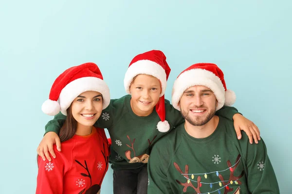 Joyeux famille en pulls de Noël et chapeaux de Père Noël sur fond de couleur — Photo