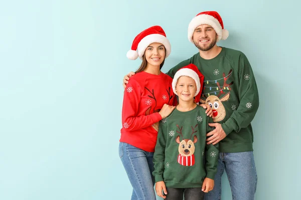 Happy family in Christmas sweaters and Santa hats on color background — Stock Photo, Image