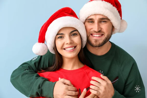 Счастливая пара в рождественских свитерах и шляпах Санты на цветном фоне — стоковое фото