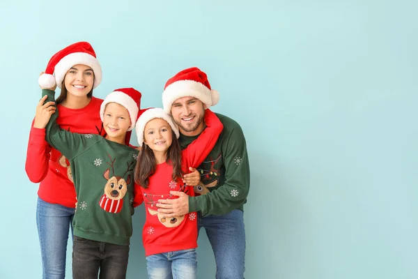 Happy family in Christmas sweaters and Santa hats on color background — Stock Photo, Image